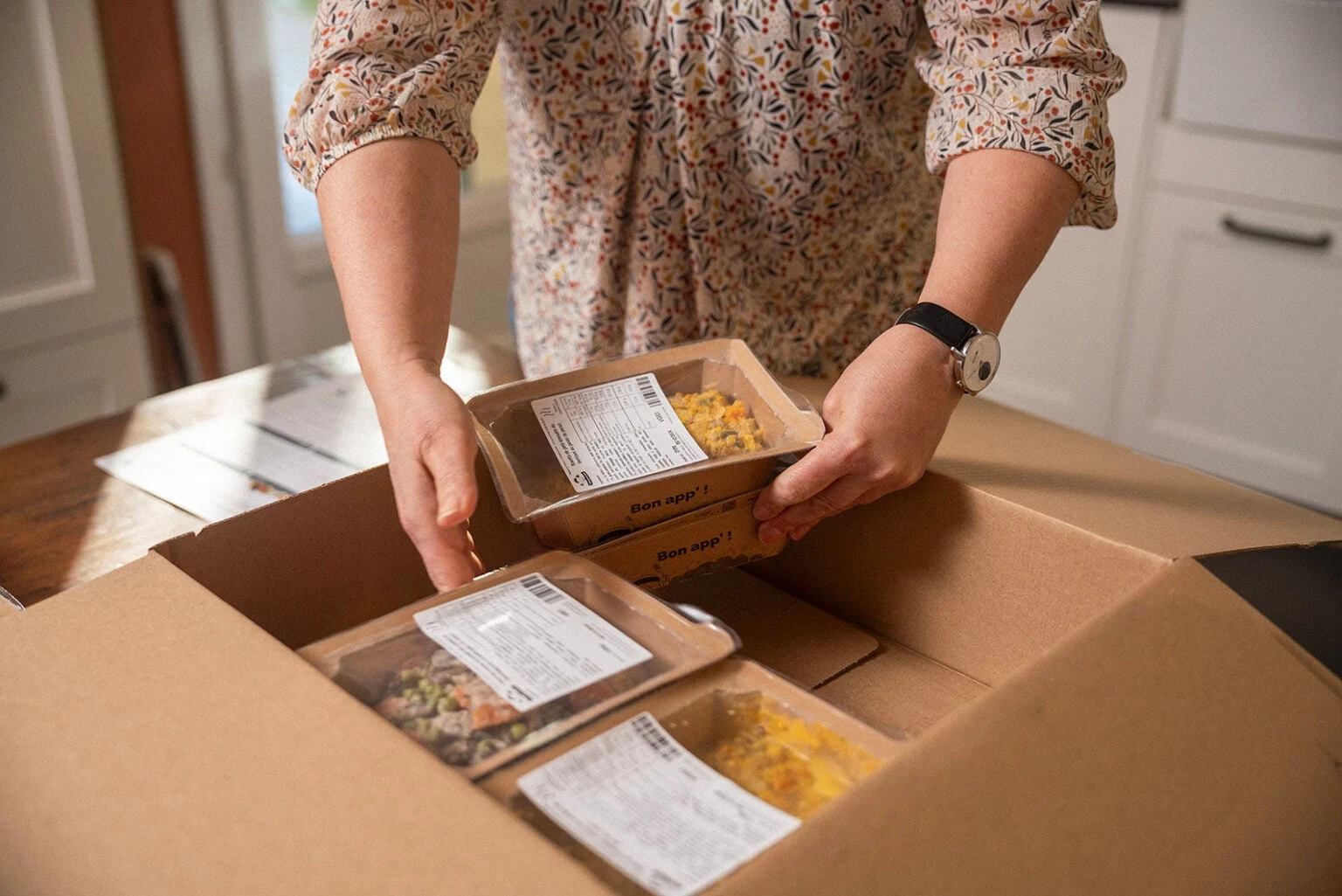 Une cliente déballe son colis La Brigade de Véro et sort des barquettes de repas frais marquées Bon app'