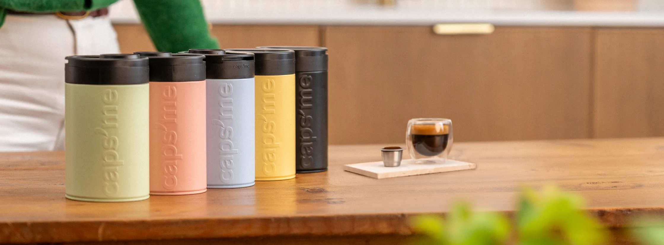 La gamme Caps'me : cinq tins de conservation colorés alignés sur une table en bois, à côté d'un espresso servi dans un verre