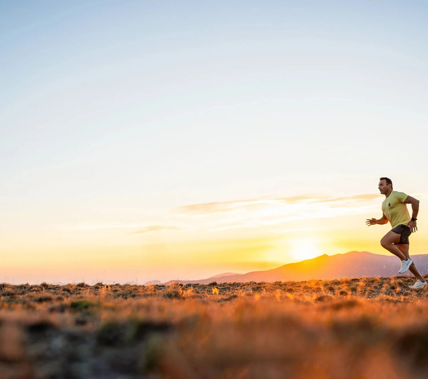 Un coureur s'élance au coucher du soleil dans un paysage de montagne